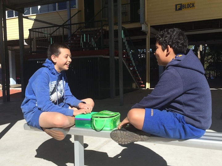 Male students eating lunch on bench in courtyard area
